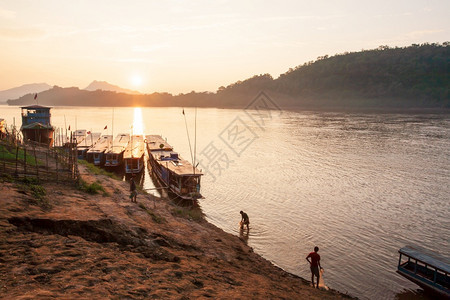 传统老挝木船在河边美丽的太阳下落蔬菜花园山地背景为SilhouetteWarmKyumLuangPrabang老挝教科文组织世界图片