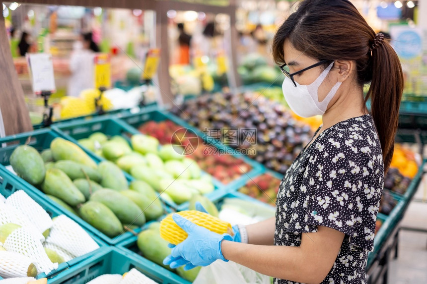 亚裔妇女佩戴硝化子手套在超市或杂货店里持有成熟的芒果保护阴阳渗透卫生新正常和19大流行后的生活亚洲人面具新冠图片