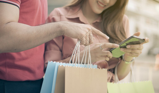 采用查看快乐的年轻顾客夫妇在购物街上走手拿着多彩的购物袋用智能手机检查销售概念和黑周五购物情况BlackFridayWessin图片