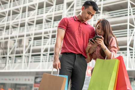 爱旅行快乐的年轻顾客夫妇在购物街上走手拿着多彩的购物袋用智能手机检查销售概念和黑周五购物情况BlackFridayWessing图片