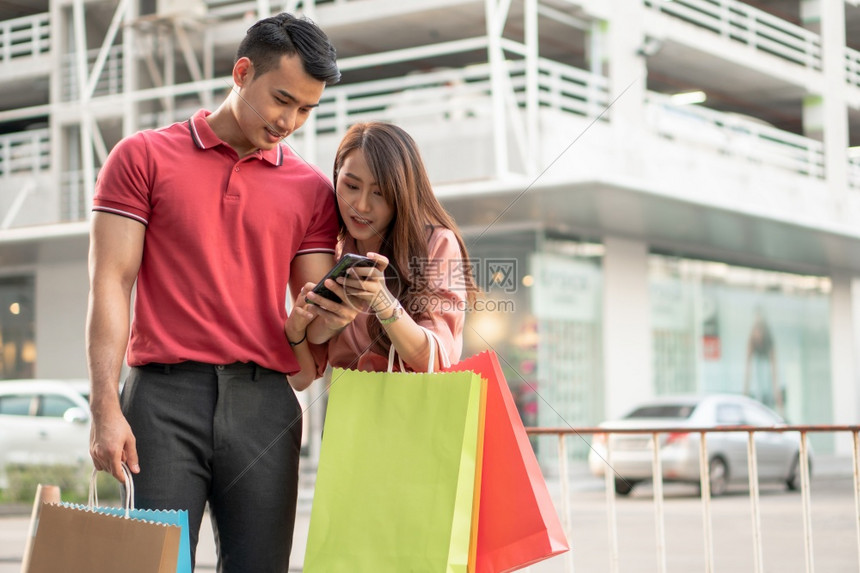 白种人步行零售快乐的年轻顾客夫妇在购物街上走手拿着多彩的购物袋用智能手机检查销售概念和黑周五购物情况BlackFridayWes图片