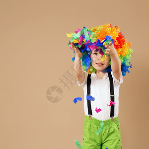 明亮的男生美丽快乐小丑男孩用大彩色假发欢快的小丑男孩用丑假跳动玩得开心孩子的肖像扔出一个多彩色的锡子和涂面生日男孩图片
