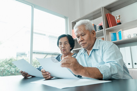 文书工作金融桌子老年夫妇使用在家里办公桌上的计算器和书面文件计算费用收入和退休后储蓄计算退休后开支和收入及储蓄退休人员财务规划和图片