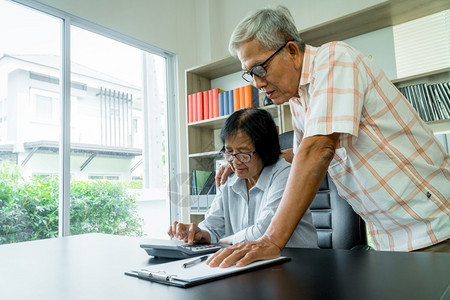 金融的屋年长老夫妇使用在家里办公桌上的计算器和书面文件计算费用收入和退休后储蓄计算退休后开支和收入及储蓄退休人员财务规划和投资概图片