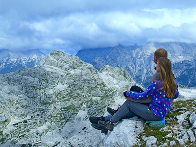 阳光心爱运动坐在悬崖上仰望天空的年轻夫妇以及看自然景观的男人和女旅行者们在山里休息观光者崇拜斯洛文尼亚阿尔卑斯山脉的地与坐在悬崖图片
