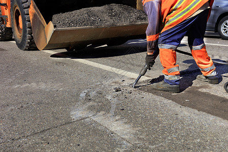 街道路维修工人在施期间用一部手推机将旧沥青从公路上的旧沥青清除出来在道路建设过程中一名工人用台充气大锤清除了一块沥青路面桶图片