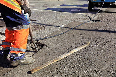 积极的黑色道路维修工人在施期间用一部手推机将旧沥青从公路上的旧沥青清除出来在道路建设过程中一名工人用台充气大锤清除了一块沥青干净图片