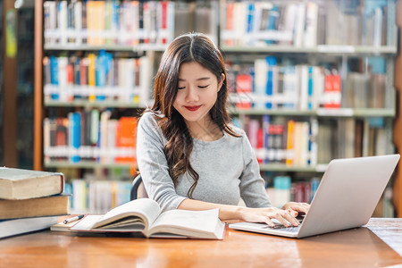 上市做功课和在大学图书馆或使用技术笔记本电脑的亚洲青年学生或具有各种书籍和文具架背景的各种群落返回学校从事家庭作业和使用技术笔记图片