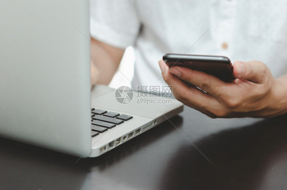 男人无线的键盘在家桌上使用智能手机和笔记本电脑搜索网上浏览互联的信息从家庭购物网络概念中工作在网上购物寻找商业信息图片