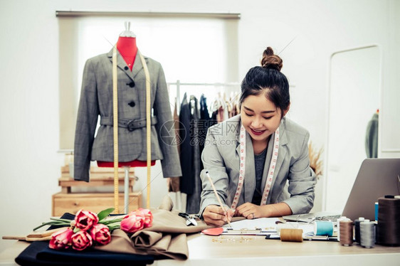 在家庭办公室讲习班上工作的有吸引力亚洲时装设计师女时装设计师在家庭办公室工作时尚妇女创造新的布料设计汇编裁缝和纫店铺吸引人的剪刀图片