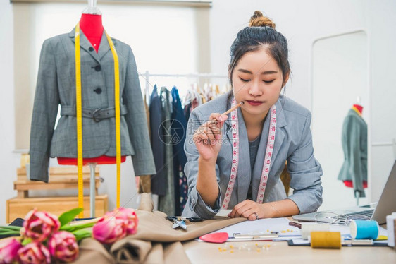 在家庭办公室讲习班上工作的有吸引力亚洲时装设计师女时装设计师在家庭办公室工作时尚妇女创造新的布料设计汇编裁缝和纫机器纺织品时髦的图片