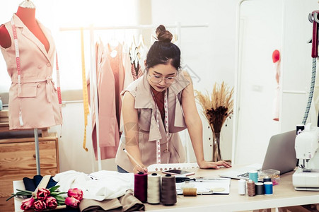 在家庭办公室讲习班上工作的有吸引力亚洲时装设计师女时装设计师在家庭办公室工作时尚妇女创造新的布料设计汇编裁缝和纫女孩收藏工作室图片