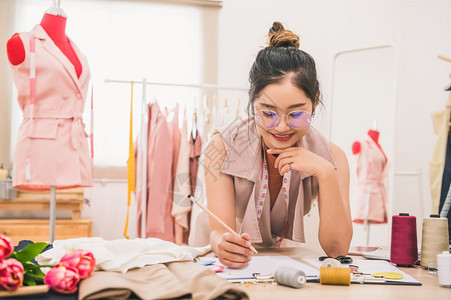 手胶带吸引人的在家庭办公室讲习班上工作的有吸引力亚洲时装设计师女时装设计师在家庭办公室工作时尚妇女创造新的布料设计汇编裁缝和纫图片