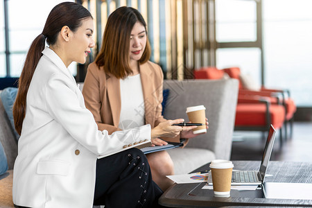 在现代办公室或合用空间的咖啡休息放松和谈话期间与伙伴企业讨论使用技术笔记本电脑的两名亚洲女商人合作伙伴和同事在新办公室或合用空间图片