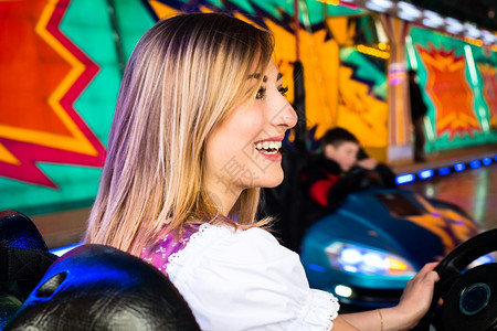 在娱乐公园的一辆电动面包车中一个美丽的女孩穿着典型德国Dirndl服装在游乐园的一辆电动保险车中背景美丽女孩身穿彩色和灯光明亮的图片