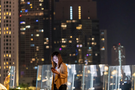 快乐的使用智能手机亚洲女商人在泰国Bangkok河边金融区地使用带微笑动作的智能移电话具有职业概念的技术在Technologyw图片