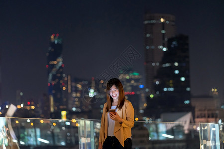 使用智能手机的亚洲女商人在泰国Bangkok河边金融区地使用带微笑动作的智能移电话具有职业概念的技术在Technologywit图片