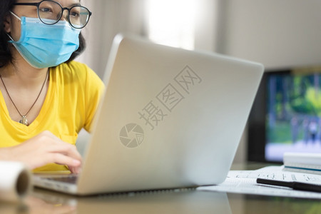 新冠办公室大流行年轻女穿着黄色衬衫和蓝外科手术面具在家工作而亚洲女则戴着眼镜与Covid19Corona的膝上型计算机Covid图片