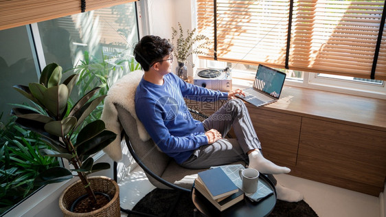 吸引人的年轻男技术使用者在膝上型计算机和看客厅远程工作或在家概念的屏幕时放松了年轻的男技术使用者轻松程度人们电脑图片
