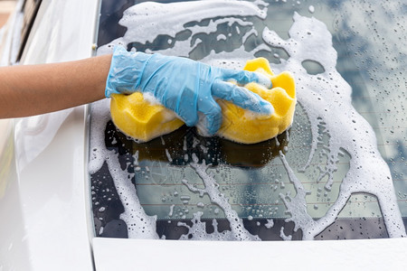 服务黄色的妇女手戴蓝套背着黄海绵洗后镜的现代汽车或清洁洗概念商业图片