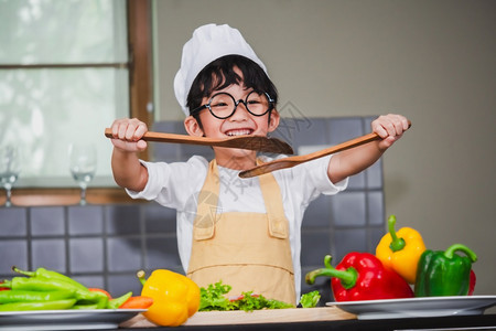 一顿饭亚洲男孩烹饪沙拉食物亚洲男孩烹煮沙拉盛着藏番茄和胡萝卜的蔬菜木勺子铃辣椒为幸福家庭做饭的快乐烤菜妈晚餐图片
