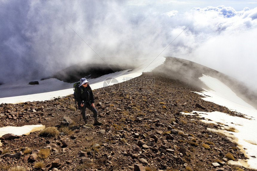 一名业余女游客背着上着一只拐杖手拿着一根拐杖在雪覆盖山的迷雾斜坡上行走一名业余女游客从山上爬到雪峰女孩士冒险图片