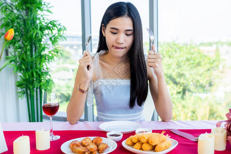 亚裔女孩感到饥饿兴奋地享受用勺子和叉包着食物与餐饮的快乐看餐厅背景桌边有酒杯和花朵红的食品在饭桌上坐着巧克力葡萄酒饮食图片