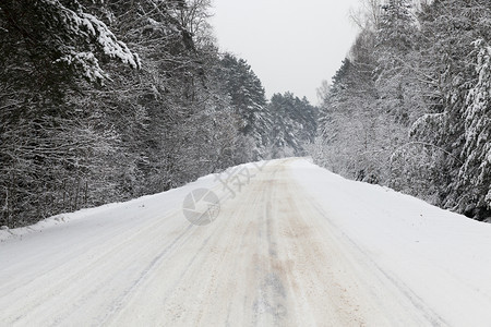 冬季在大雪降下拍摄到的冬季柏油路在雪下穿过森林的冬季公路上转弯而过然后在寒雪下经过场景冬天风图片