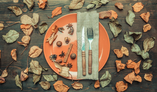 邀请植物橙秋的成份多彩叶子在盘上围着刀和叉坚果肉桂和丁香图片
