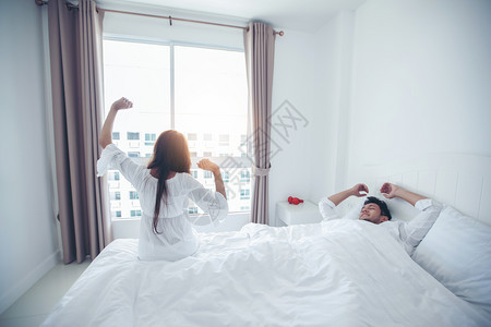 在室内得到女士床上醒来的情侣在床上完全休息早打开窗帘以呼吸新鲜空气清晨打开窗帘图片
