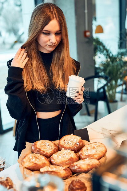 肖像热的员工女人拿着杯子喝咖啡看着糕点面包蛋和饼干等待命令女孩购买甜食和热饮让在咖啡店买东西的年轻女青可以休息去图片