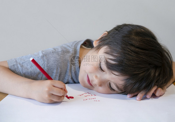 课爱创造力小男孩倒在桌子上给妈画红心的表情这小男孩躺在桌子上为妈画出红心他写了一张脸像快乐的孩子向母亲写短信学龄前孩子用红色写作图片