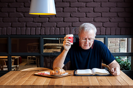 拼盘灯男人坐在桌子上咖啡和羊角面包在小吃酒吧里阅读圣经用于物质和精神喂养的课间工作休闲的图片