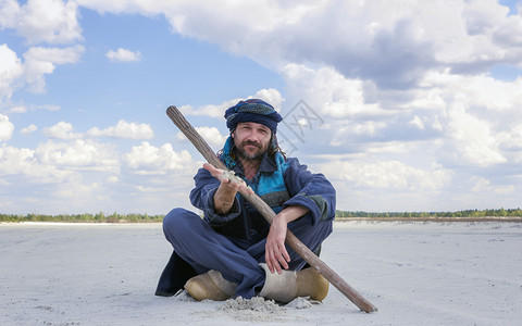 脸男人穿着缠头巾和族裔服装的微笑型男子在夏日蓝天下坐在沙漠中的蓝天空下沙漠地带时用手展示白色沙子重点突出概念图像带有复制空间高级图片