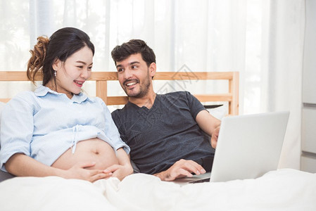 快乐的男子及其怀孕妻使用笔记本电脑搜索新生儿婴用品以准备为人父母的新生儿物品家庭与技术概念妇女健康和医疗主题妇女保健医疗的肚子图片