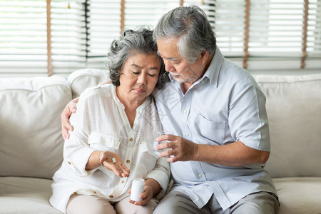 尽管担心关老人安慰妻子而她却有一位冷酷的老年妇女在家中发烧和坐沙疾病科罗纳毒Covid19检疫时手持药丸或品图片