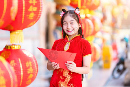 保持身着青山传统红衣装饰的亚裔女孩手握红色信封和灯笼上面写着中文字祝福是新年的分节日钱背景图片