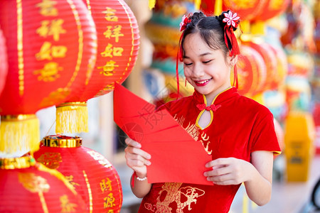 祝贺女可爱的身着青山传统红衣装饰的亚裔女孩手握红色信封和灯笼上面写着中文字祝福是新年的分图片
