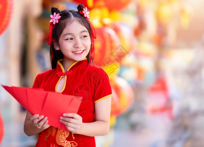 身着青山传统红衣装饰的亚裔女孩手握红色信封和灯笼上面写着中文字祝福是新年的分书面奖金幸运的背景图片