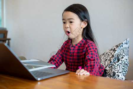 亚洲女孩或儿利用笔记本和技术在学校假期间线学习和家里看漫画进行家庭教育概念和活动亚洲女孩或儿使用笔记及技术在学校放假期间线学习和图片