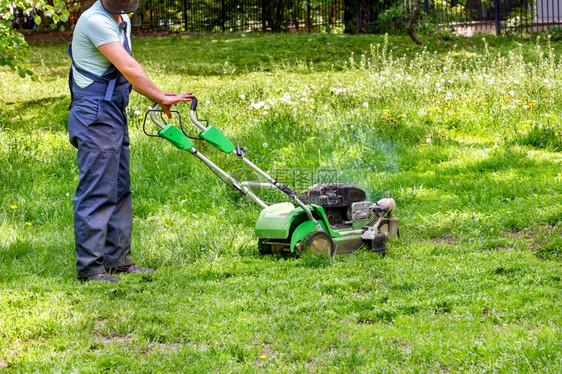 公园穿蓝衣的用工人照顾绿草坪使用汽油割草机身穿蓝服的工人用业油采草机砍伐绿城市的剪机图片