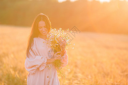 喜悦户外洋甘菊小麦田中的美貌佳人在日落时盛满一束香菊花小麦田中美丽的女士手拿着成熟的麦子图片