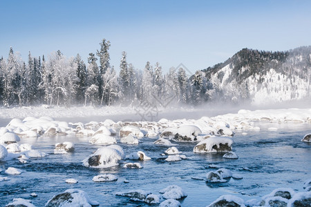 抽象的黄昏多雾路段河流岸上的岩石和树木被雪覆盖冰了下满是积雪图片