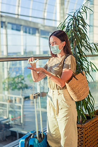 为预防国际机场的而面戴罩的旅游妇女在公共场所使用洗手剂以保护和疾在公共场所使用防毒剂保护病和疾在国际机场戴医疗面具的旅游青年妇女图片