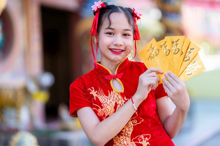 穿着红色传统青山装饰的可爱小亚洲女孩肖像拿着黄信封上面写着中文字祝福是新年节的幸运日啊中华新年节的钱黄色图片