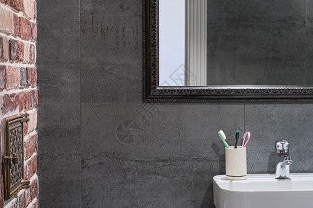 灯光内部详细信息中灰色瓷石器砖墙和水槽上方的镜子时髦浴室内个人卫生用品气氛下沉图片
