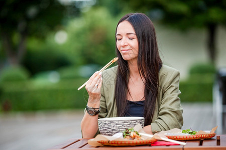 离开在户外咖啡厅吃亚洲街边食物的年轻美女吃饭的年轻子在街上抢走面条小工具年轻的图片