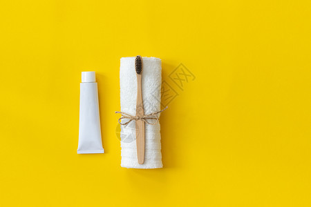 白色毛巾上天然生态友好的竹子刷和牙膏套针管用于在纸黄色背景张上洗涤黄皮笔用色胶布和牙膏套管上天然生态友好的竹子刷文本或设计用牙膏图片