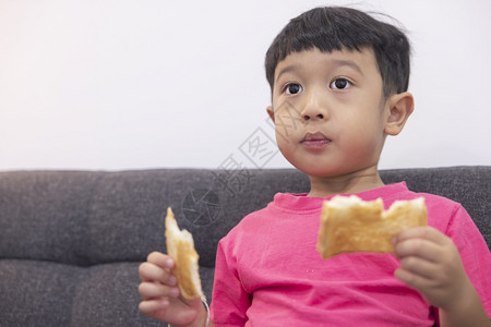 愉快乐趣情感微笑的小男孩吃面包在客厅舒适的沙发上看电视在数字智能电视上玩游戏时享受快乐小男孩用美味甜点欢乐图片