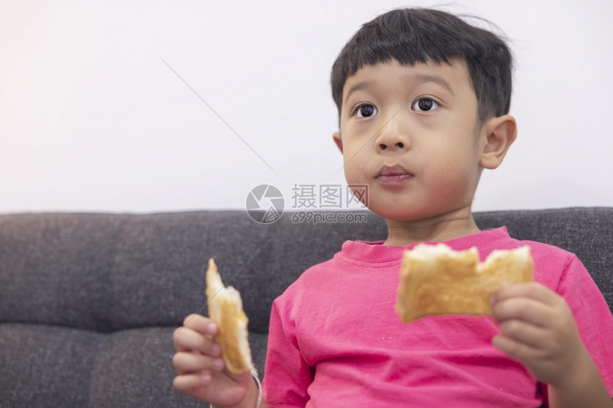 愉快乐趣情感微笑的小男孩吃面包在客厅舒适的沙发上看电视在数字智能电视上玩游戏时享受快乐小男孩用美味甜点欢乐图片